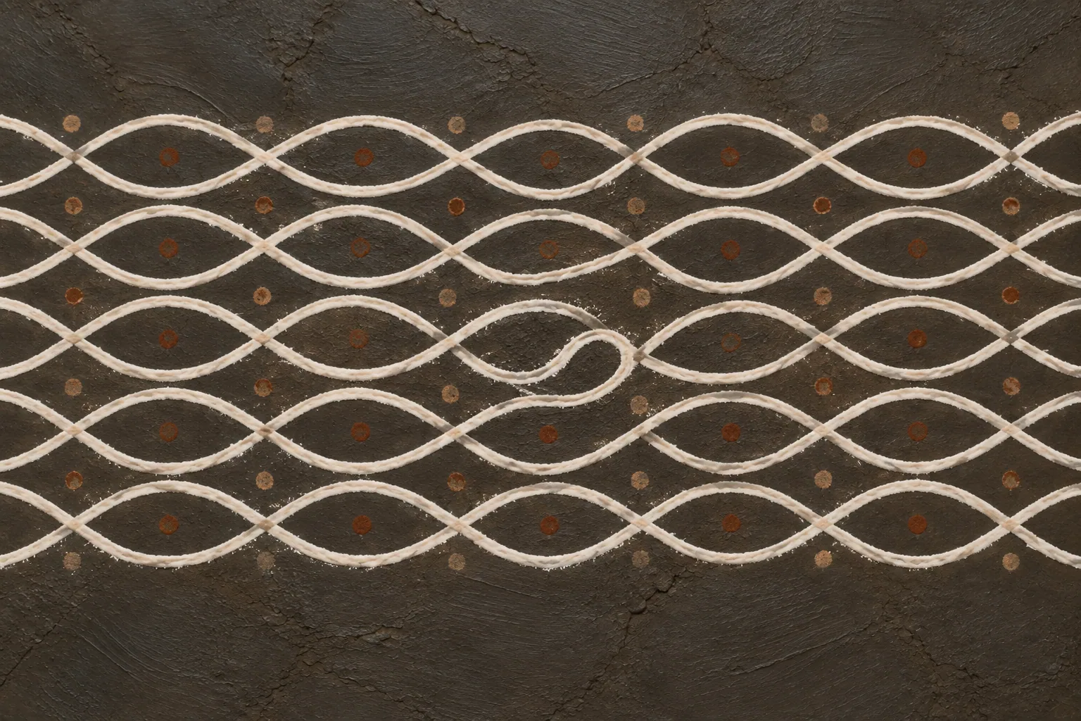A close view of a white looping line pattern on dark clay, perfectly regular except for one loop drawn the wrong way.